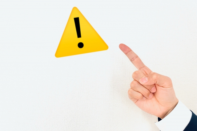 注意マークを指差す手。注意点を示すイメージ。