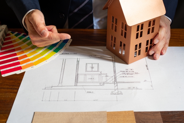 設計図と家の模型を前に説明する様子。