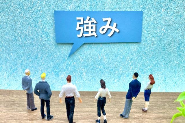 「強み」と書かれた吹き出しを見上げる人物のミニチュア