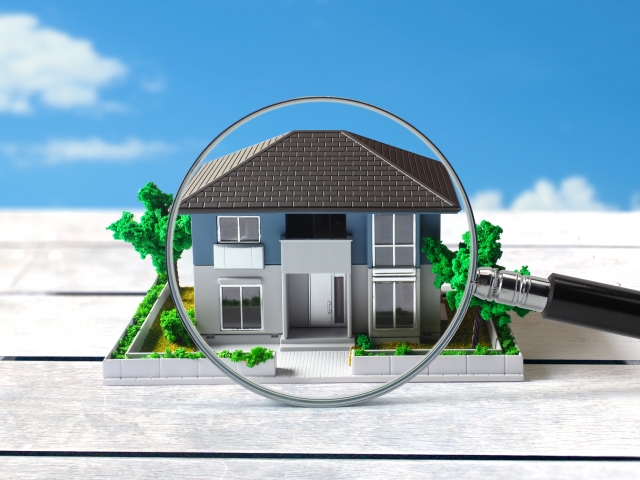 虫眼鏡で拡大された住宅模型。物件調査を示すイメージ。