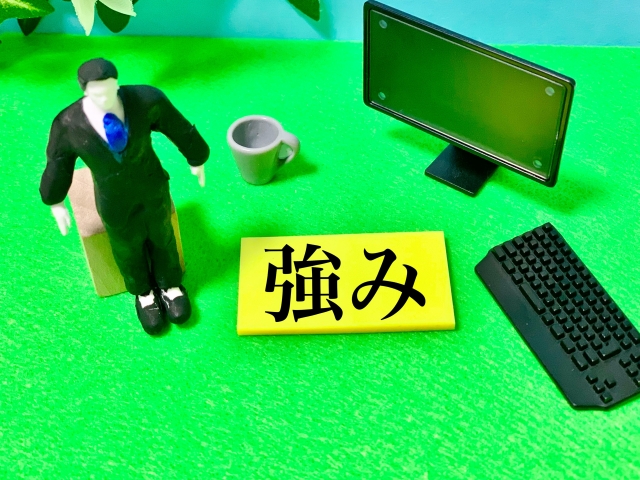 ミニチュアの男性とパソコン横に置かれた「強み」のカード