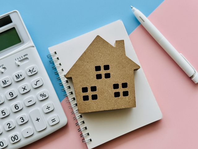 電卓とノートの上に置かれた住宅模型