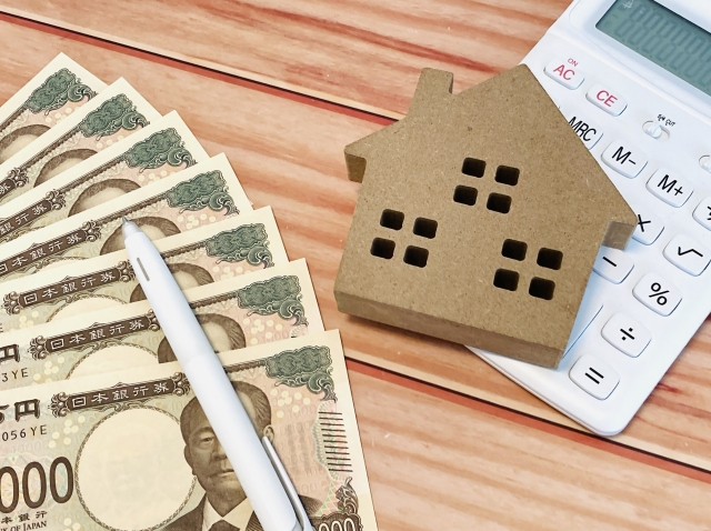 紙幣と電卓、家の模型。住宅ローンや資金計算をイメージした写真。