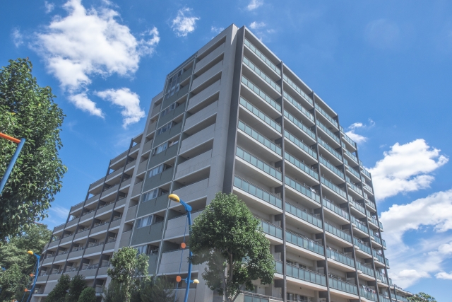 青空の下に建つ高層マンション。集合住宅を示すイメージ。