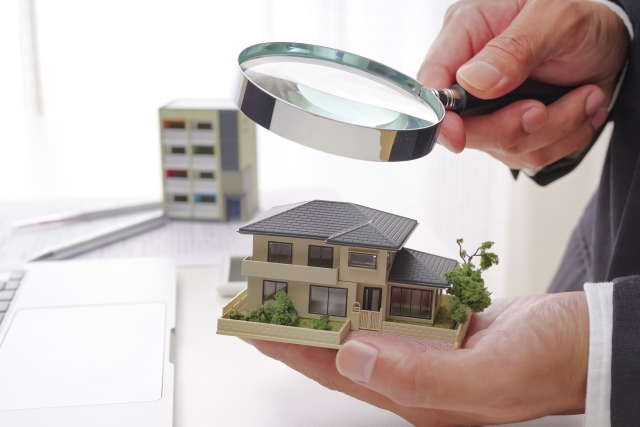虫眼鏡で住宅模型を確認する手元