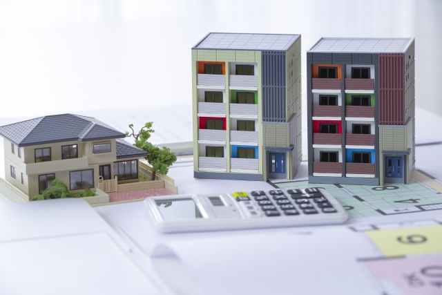 戸建てとマンション模型を図面と電卓の上に置いたイメージ