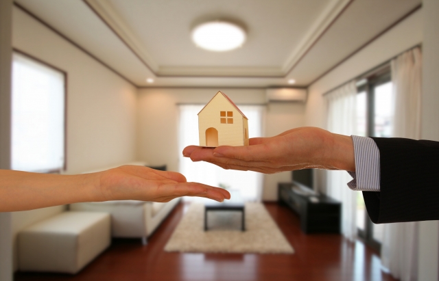 家の模型を手から手へ渡す様子。住宅の引き渡しを示すイメージ。