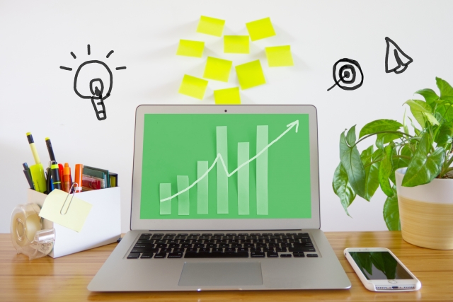 ノートパソコン画面に表示された右肩上がりのグラフとデスク周りの様子